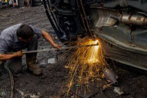 Home Mechanic welding a car frame outdoors, producing dramatic sparks and intense focus.
