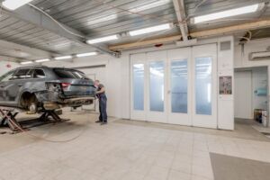 Mechanic repairing a car indoors at an auto workshop, focusing on vehicle maintenance.